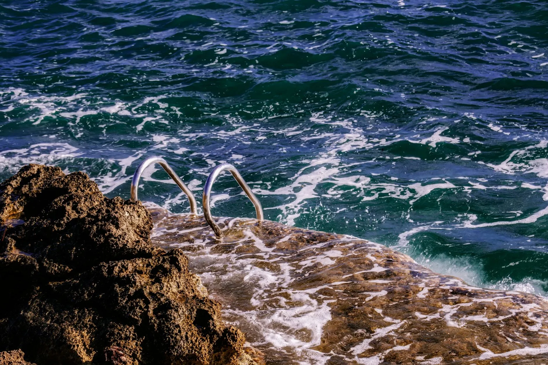 Échelle en inox plongeant dans une mer agitée depuis une dalle de rocher