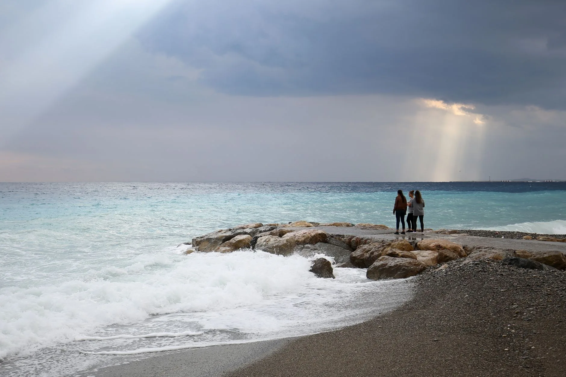 Mer agitée sur une plage de galets, avec une digue de rochers au large